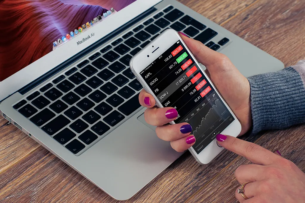 A hand holding a phone with a booking app above a laptop